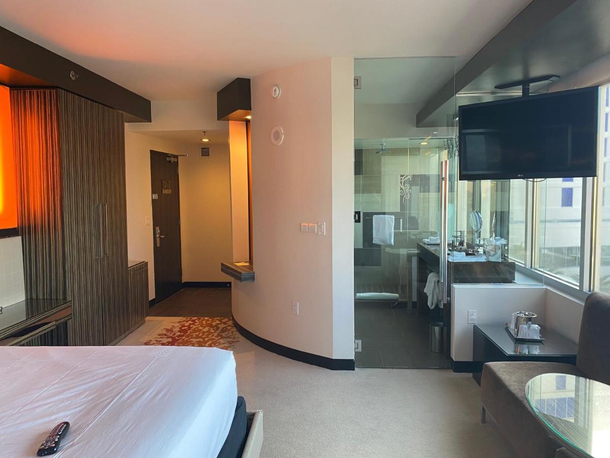 Hard Rock Hotel & Casino בילוקסי מראה חיצוני תמונה The photo shows a modern hotel room. On the left side, there is a bed with white bedding, and the headboard area features warm lighting. The room has a window that allows natural light to come in, offering a view of the outside. On the right side, th